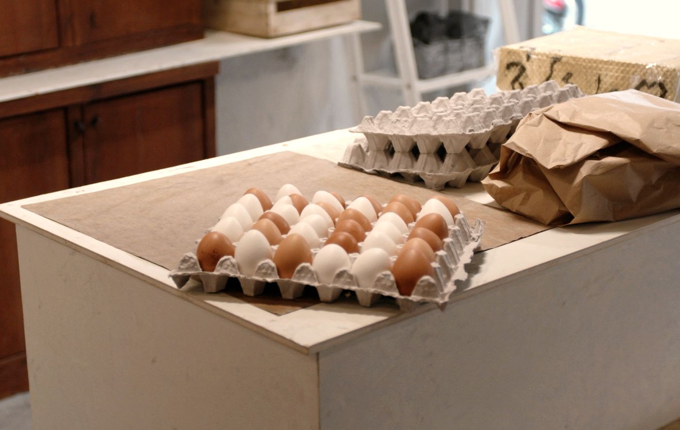 A flat of thirty brown and white eggs open on the store counter, with a stack of empty grey pulp cartons and a folded paper sack beside it.